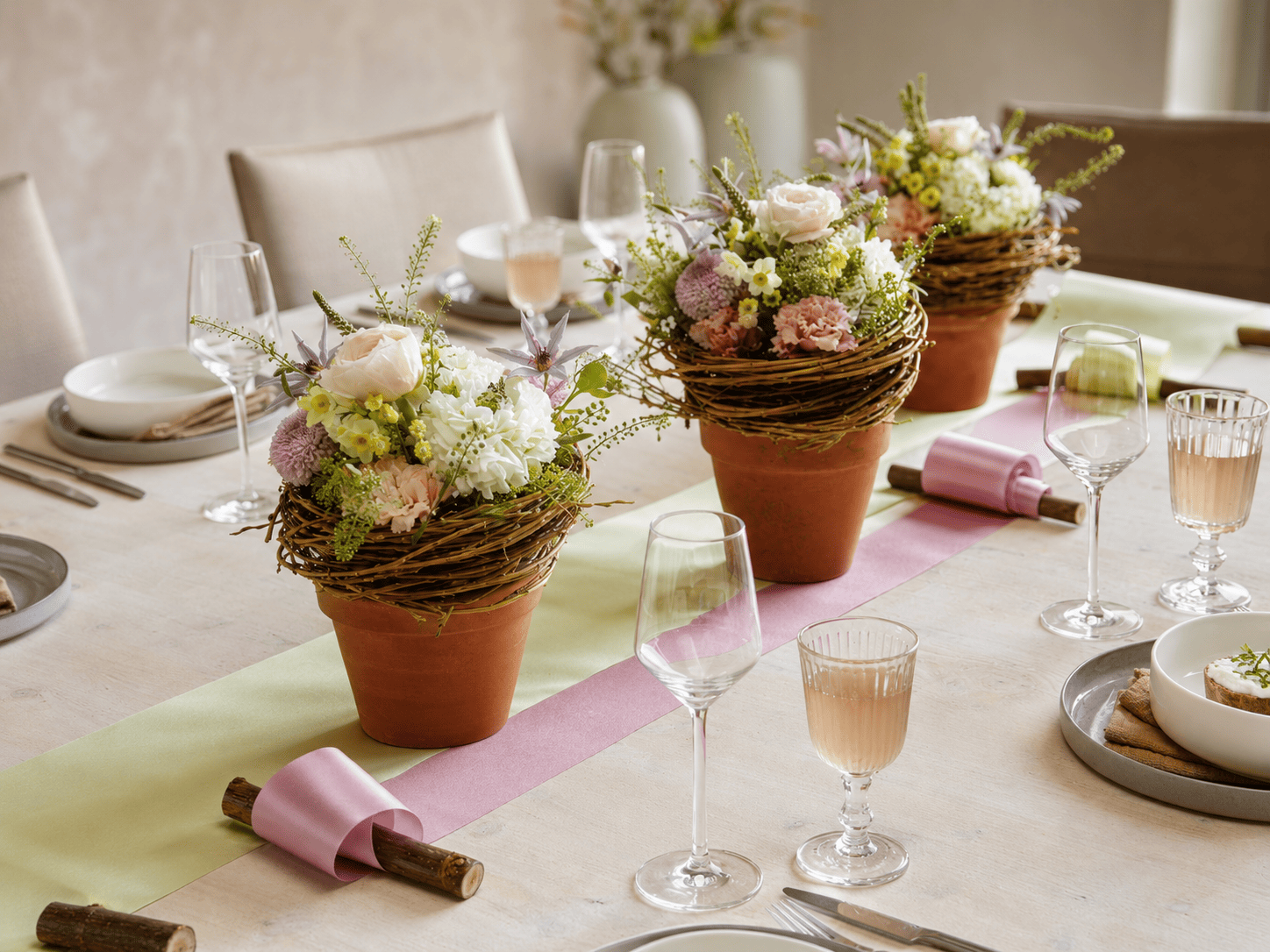 Gedeckte Tafel mit floralen Gestecken sowie rosa und hellgrünem Satin-Kranzband